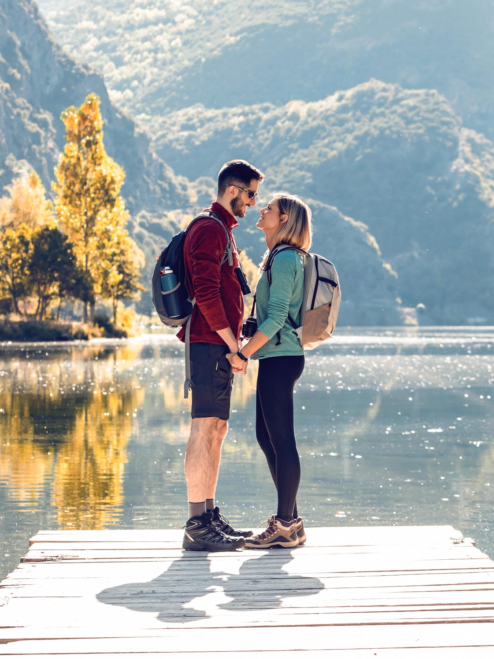 Verliebtes Paar auf einem Holzsteg am See mit bewaldeten Bergen im Hintergrund