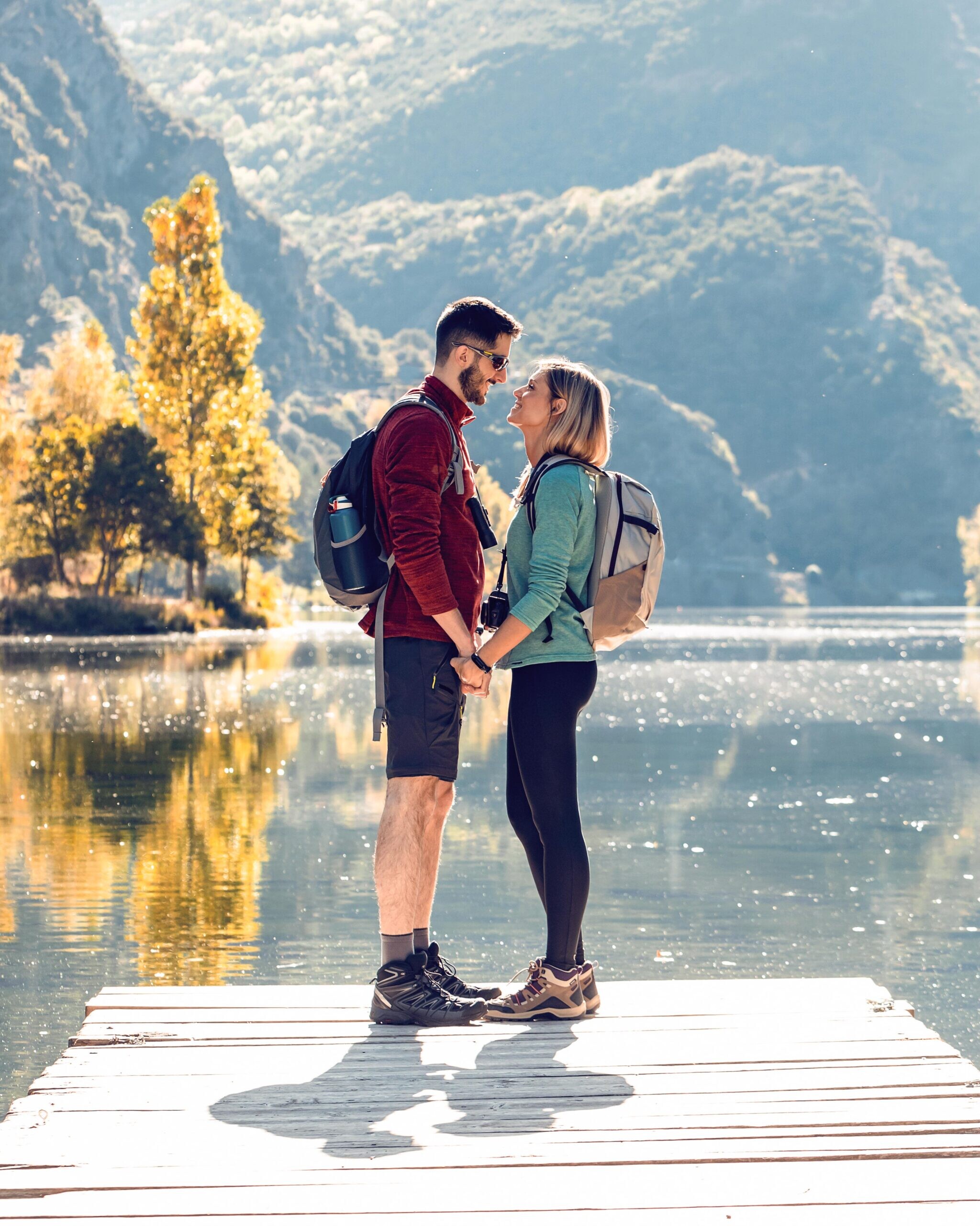 Verliebtes Paar auf einem Holzsteg am See mit bewaldeten Bergen im Hintergrund