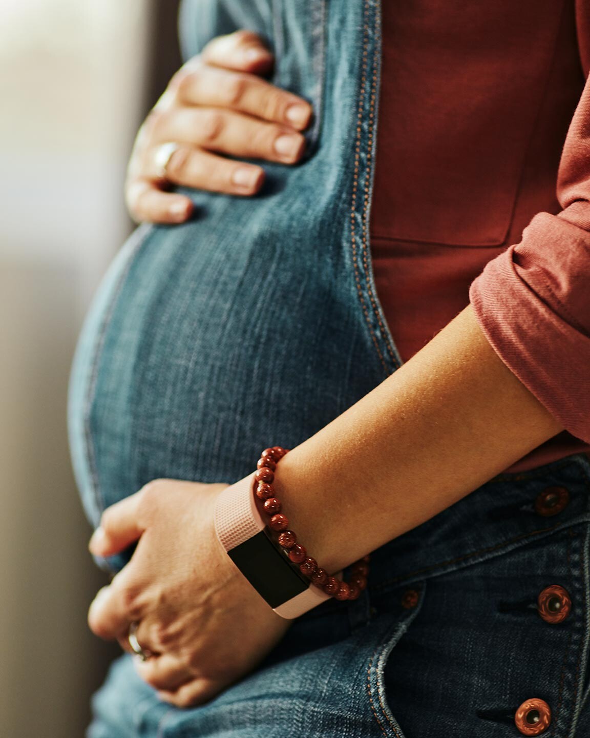 Eine schwangere Frau hält behutsam die Hände auf ihren Bauch und trägt eine Jeans Latzhose