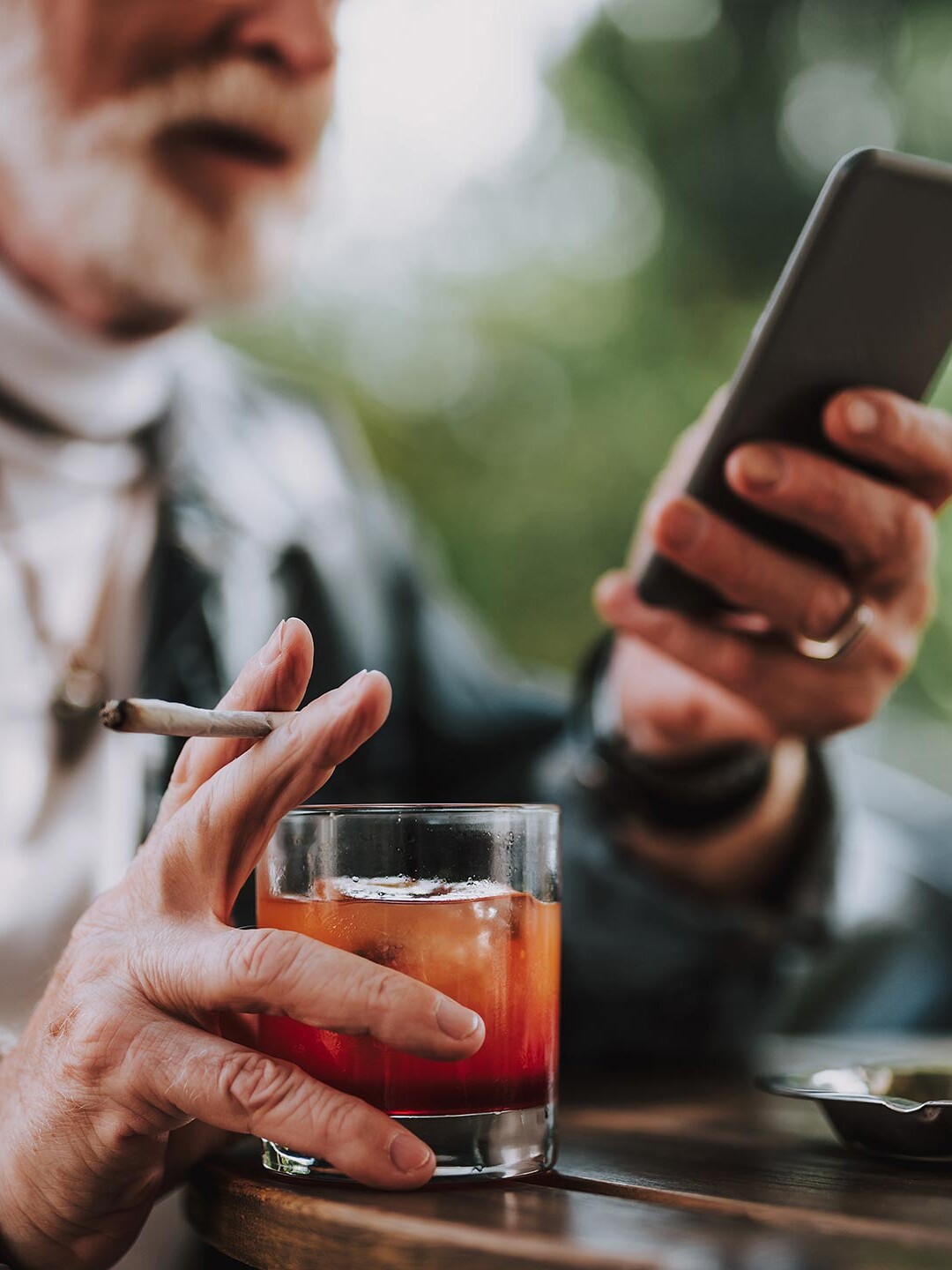 Älterer Mann mit Smartphone, Whisky und Zigarette