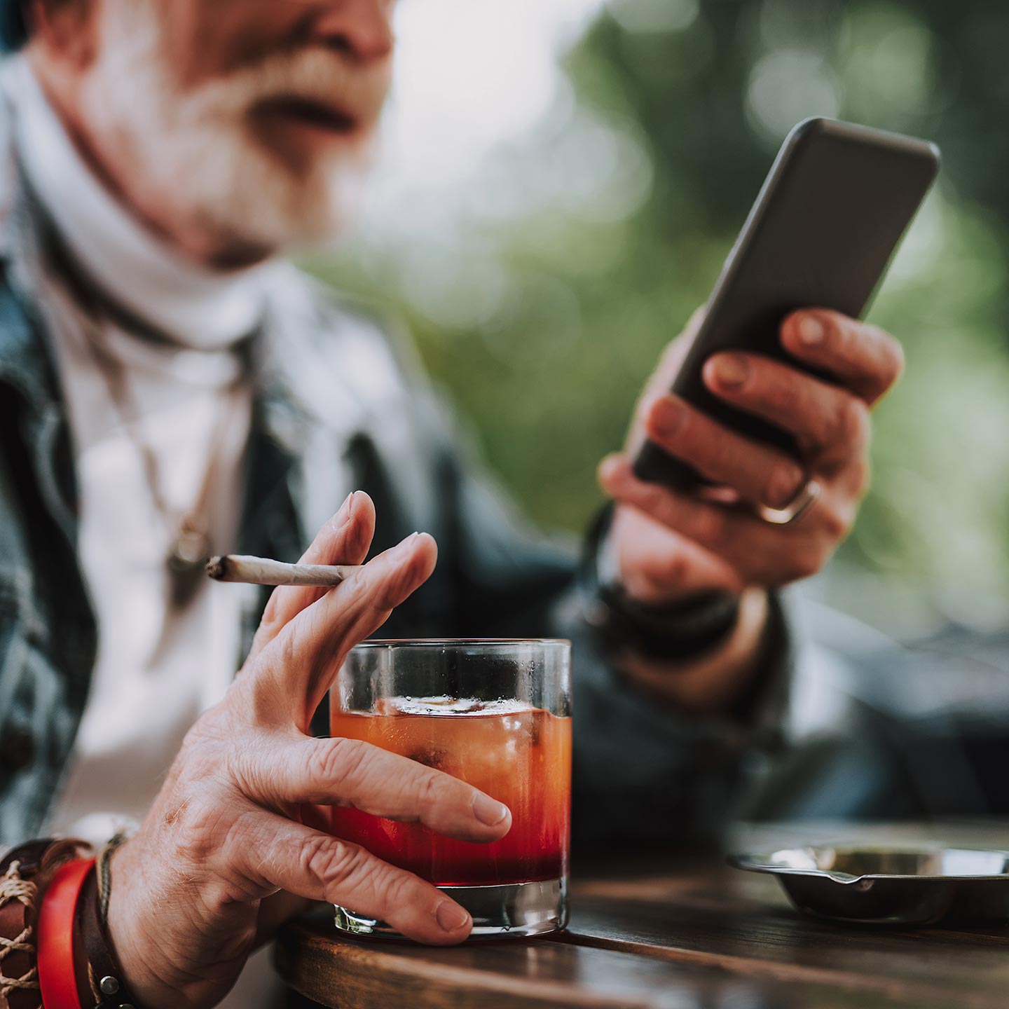 Älterer Mann mit Smartphone, Whisky und Zigarette