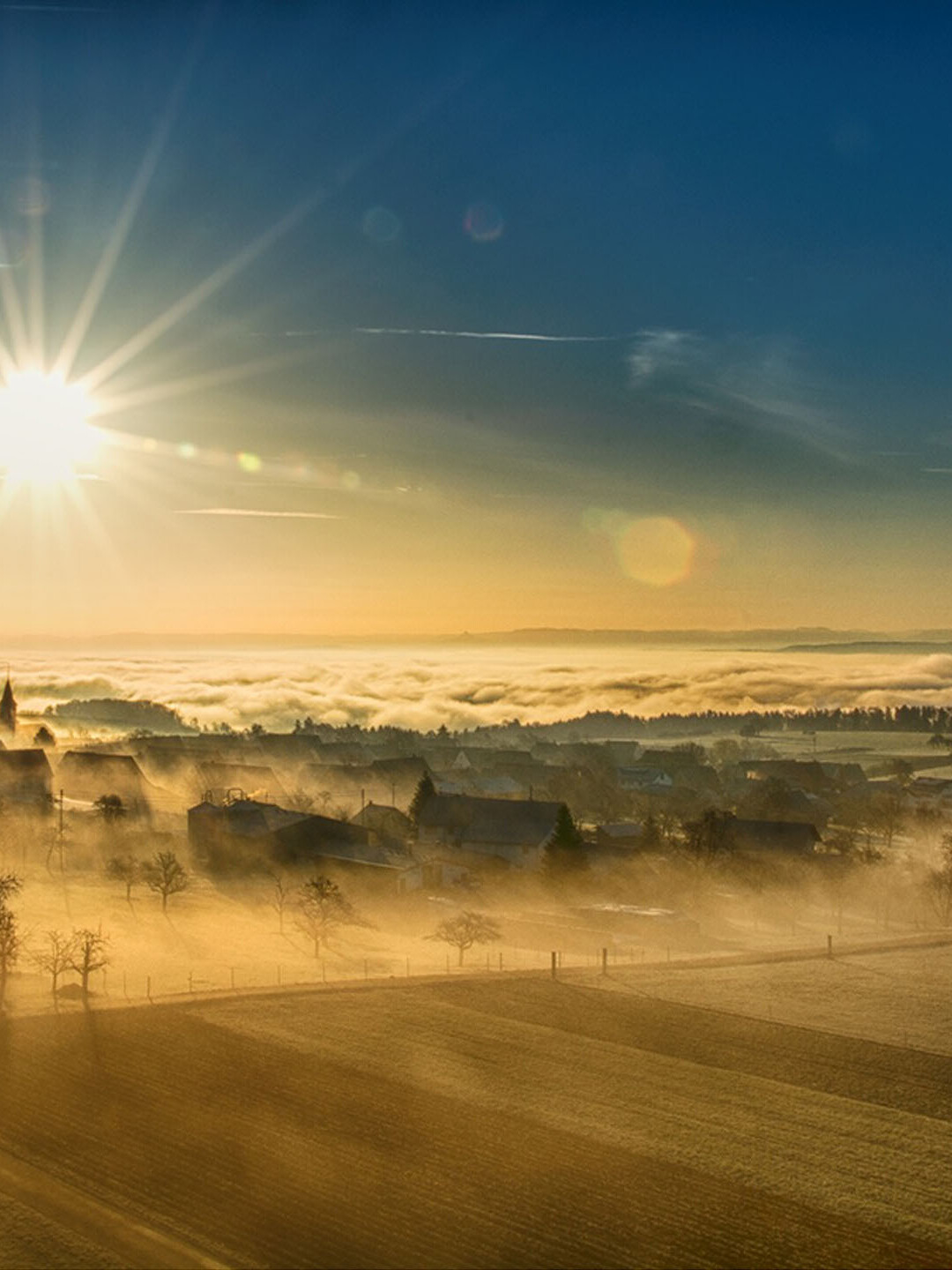 Die Sonne geht im Winter über einem Nebelbedeckten Dorf auf