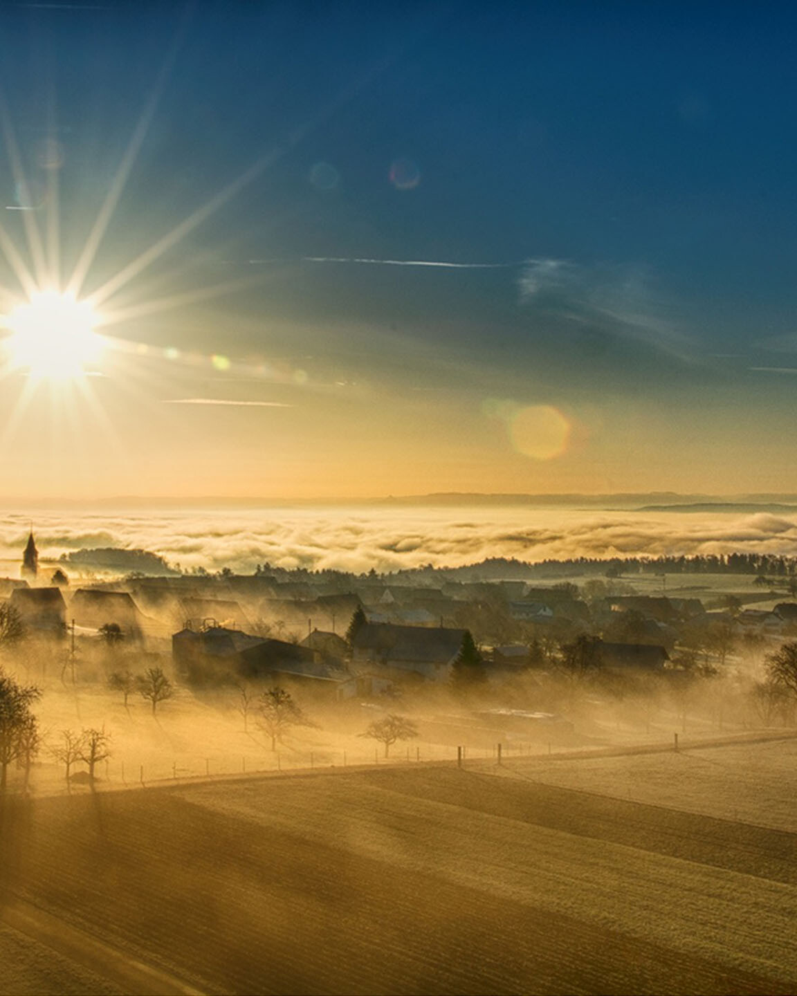 Die Sonne geht im Winter über einem Nebelbedeckten Dorf auf